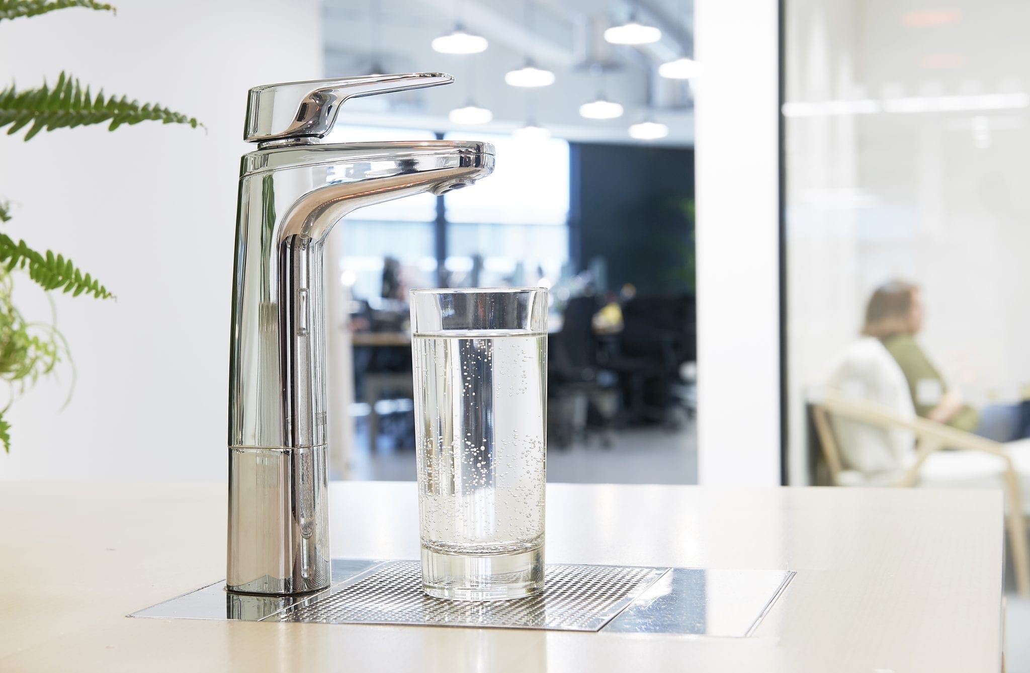 Chrome XL dispenser on riser and font with glass of sparkling water